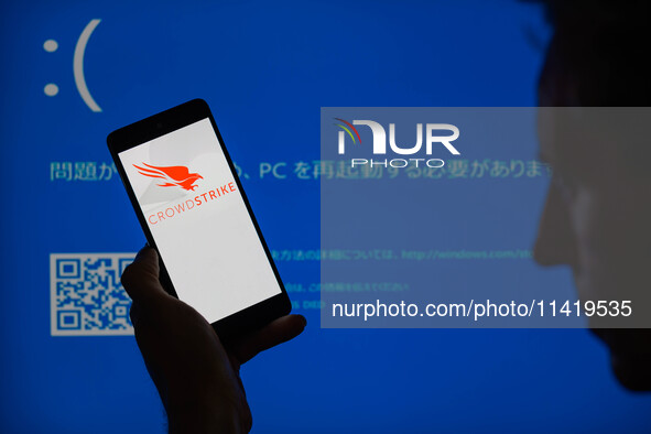 The CrowdStrike logo is being displayed on a smartphone with a Windows blue screen visible in the background in this photo illustration in B...