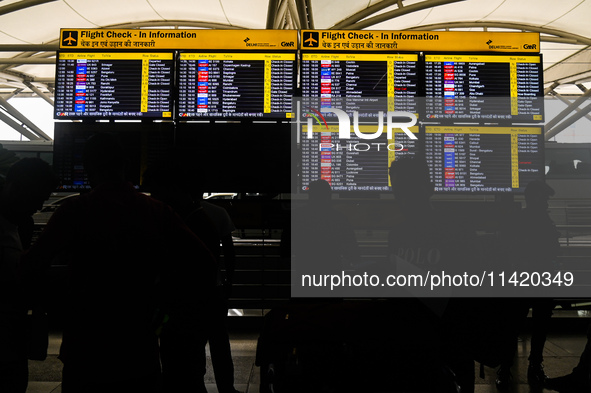 People are looking at the screens displaying flight details amid a global Microsoft outage at the Indira Gandhi International (IGI) Airport,...