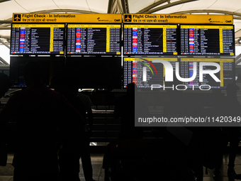 People are looking at the screens displaying flight details amid a global Microsoft outage at the Indira Gandhi International (IGI) Airport,...