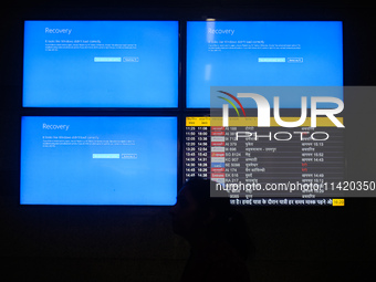 People are moving past screens displaying error messages amid a global Microsoft outage at the Indira Gandhi International (IGI) Airport, in...