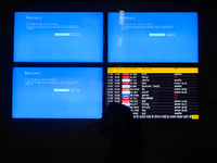 People are moving past screens displaying error messages amid a global Microsoft outage at the Indira Gandhi International (IGI) Airport, in...