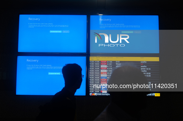 People are moving past screens displaying error messages amid a global Microsoft outage at the Indira Gandhi International (IGI) Airport, in...