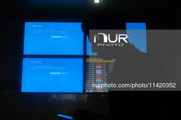 People are moving past screens displaying error messages amid a global Microsoft outage at the Indira Gandhi International (IGI) Airport, in...