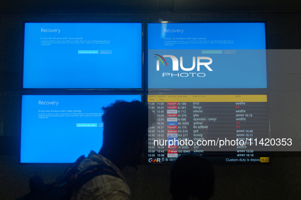 People are moving past screens displaying error messages amid a global Microsoft outage at the Indira Gandhi International (IGI) Airport, in...