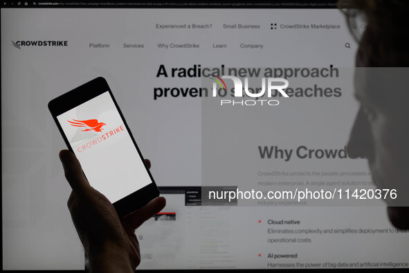 The CrowdStrike logo is being displayed on a smartphone with the CrowdStrike web page visible in the background in this photo illustration i...