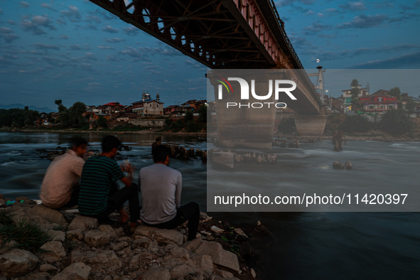 People are enjoying the cool breeze on the banks of the river Jhelum in Sopore, Jammu and Kashmir, India, on July 19, 2024. 