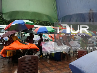 A shopkeeper is covering plastics and coloring umbrellas in rain showers in Kolkata, India, on July 19, 2024. (