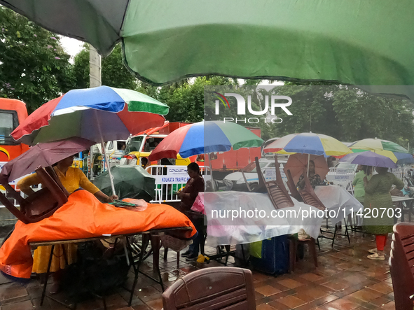 A shopkeeper is covering plastics and coloring umbrellas in rain showers in Kolkata, India, on July 19, 2024. 