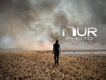 A protester is walking towards a wildfire started by a launched tear gas canister during a march as part of a rally against the construction...