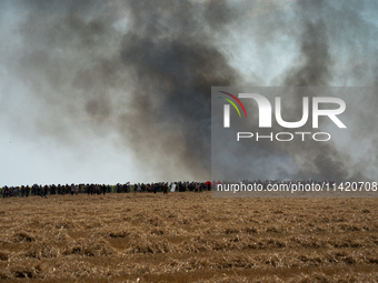 Protesters are walking past a wildfire started by a launched tear gas canister during a march as part of a rally against the construction of...