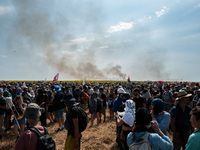 Protesters are walking past a wildfire started by a launched tear gas canister during a march as part of a rally against the construction of...