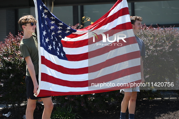 Two kids are holding up an American flag at the funeral procession. Bystanders are gathering for the funeral procession of Corey Comperatore...