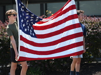 Two kids are holding up an American flag at the funeral procession. Bystanders are gathering for the funeral procession of Corey Comperatore...