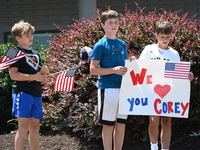 Children are holding up a sign that reads ''We Love You Corey'' at the funeral procession. Bystanders are gathering for the funeral processi...