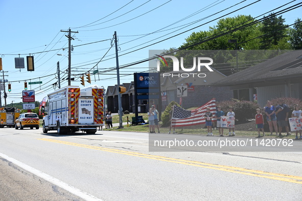 A fire engine is carrying the casket of Corey Comperatore during the funeral procession. Bystanders are gathering for the funeral procession...