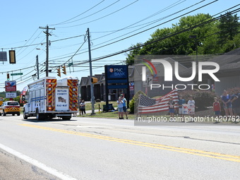 A fire engine is carrying the casket of Corey Comperatore during the funeral procession. Bystanders are gathering for the funeral procession...