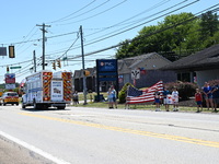 A fire engine is carrying the casket of Corey Comperatore during the funeral procession. Bystanders are gathering for the funeral procession...