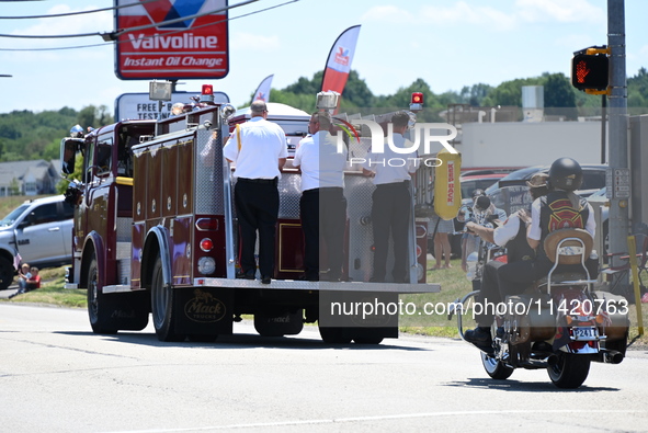 A fire engine is carrying the casket of Corey Comperatore during the funeral procession. Bystanders are gathering for the funeral procession...