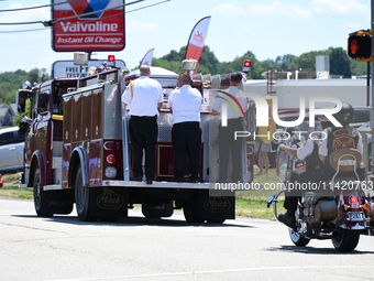 A fire engine is carrying the casket of Corey Comperatore during the funeral procession. Bystanders are gathering for the funeral procession...