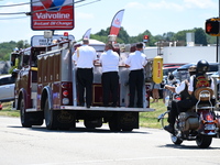 A fire engine is carrying the casket of Corey Comperatore during the funeral procession. Bystanders are gathering for the funeral procession...