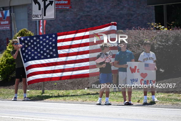 Bystanders are gathering and holding up signs and American flags for the funeral procession of Corey Comperatore in Sarver, Pennsylvania, Un...