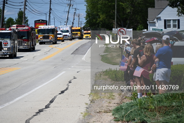 Bystanders are gathering and holding up signs and American flags for the funeral procession of Corey Comperatore in Sarver, Pennsylvania, Un...