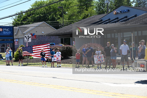 Bystanders are gathering and holding up signs and American flags for the funeral procession of Corey Comperatore in Sarver, Pennsylvania, Un...