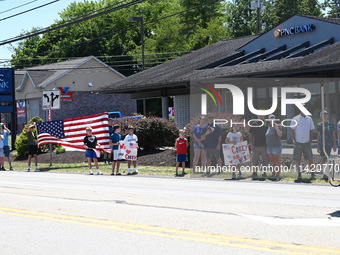 Bystanders are gathering and holding up signs and American flags for the funeral procession of Corey Comperatore in Sarver, Pennsylvania, Un...