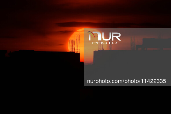 A bird is flying past the sun as it is going down behind the buildings in Guwahati, India, on July 20, 2024. 