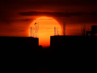 A bird is flying past the sun as it is going down behind the buildings in Guwahati, India, on July 20, 2024. (