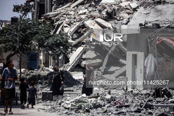 Palestinians are walking in front of a building damaged by Israeli bombardment in Nuseirat in the central Gaza Strip, on July 21, 2024, amid...