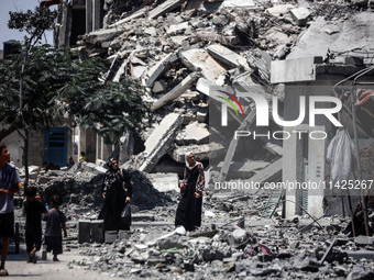 Palestinians are walking in front of a building damaged by Israeli bombardment in Nuseirat in the central Gaza Strip, on July 21, 2024, amid...