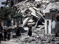 Palestinians are walking in front of a building damaged by Israeli bombardment in Nuseirat in the central Gaza Strip, on July 21, 2024, amid...