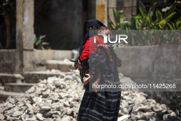 A displaced Palestinian woman is cuddling her baby and walking in front of a building damaged by Israeli bombardment in Nuseirat in the cent...