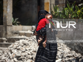 A displaced Palestinian woman is cuddling her baby and walking in front of a building damaged by Israeli bombardment in Nuseirat in the cent...