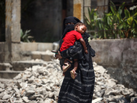 A displaced Palestinian woman is cuddling her baby and walking in front of a building damaged by Israeli bombardment in Nuseirat in the cent...