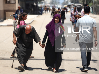 Palestinians are walking in front of a building damaged by Israeli bombardment in Nuseirat in the central Gaza Strip, on July 21, 2024, amid...