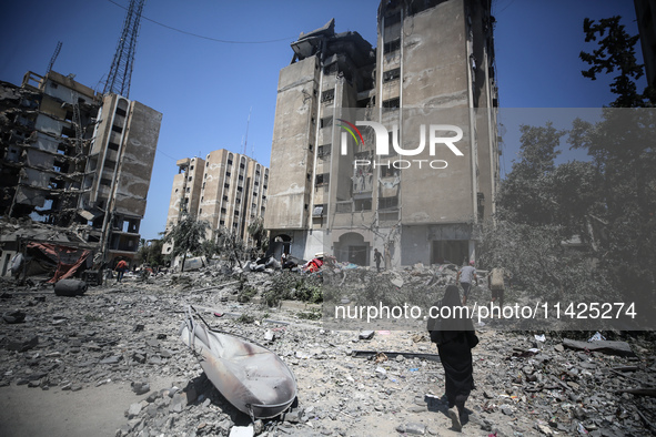 Palestinians are walking in front of a building damaged by Israeli bombardment in Nuseirat in the central Gaza Strip, on July 21, 2024, amid...