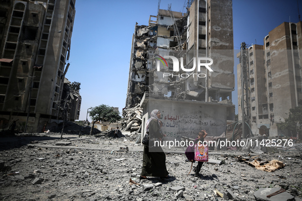 Palestinians are walking in front of a building damaged by Israeli bombardment in Nuseirat in the central Gaza Strip, on July 21, 2024, amid...