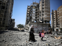 Palestinians are walking in front of a building damaged by Israeli bombardment in Nuseirat in the central Gaza Strip, on July 21, 2024, amid...