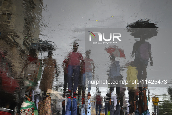 People are walking on the street reflected in a puddle of rainwater in the monsoon in Kolkata, India, on July 21, 2024. 