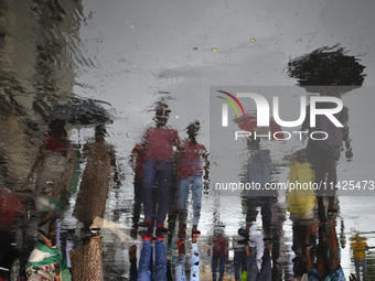 People are walking on the street reflected in a puddle of rainwater in the monsoon in Kolkata, India, on July 21, 2024. (