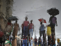 People are walking on the street reflected in a puddle of rainwater in the monsoon in Kolkata, India, on July 21, 2024. (