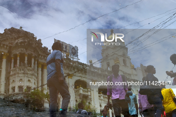 People are walking on the street reflected in a puddle of rainwater in the monsoon in Kolkata, India, on July 21, 2024. 