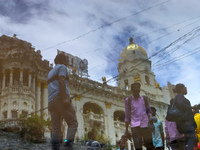 People are walking on the street reflected in a puddle of rainwater in the monsoon in Kolkata, India, on July 21, 2024. (