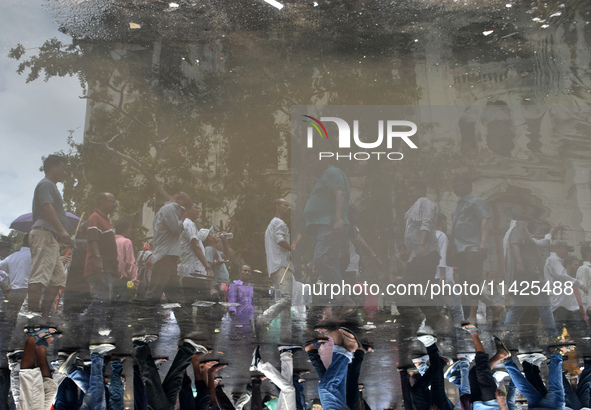 People are walking on the street reflected in a puddle of rainwater in the monsoon in Kolkata, India, on July 21, 2024. 