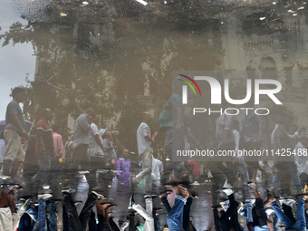 People are walking on the street reflected in a puddle of rainwater in the monsoon in Kolkata, India, on July 21, 2024. (