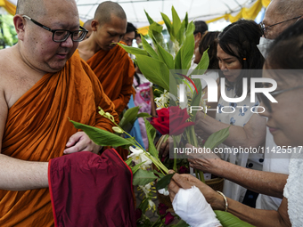 Thais are offering flowers to Buddhist monks during a floral merit-making ceremony, known as 'tak bat dok mai', at Rama IX Golden Jubilee Te...