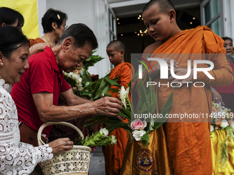 Thais are offering flowers to Buddhist monks during a floral merit-making ceremony, known as 'tak bat dok mai', at Rama IX Golden Jubilee Te...