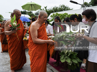 Thais are offering flowers to Buddhist monks during a floral merit-making ceremony, known as 'tak bat dok mai', at Rama IX Golden Jubilee Te...